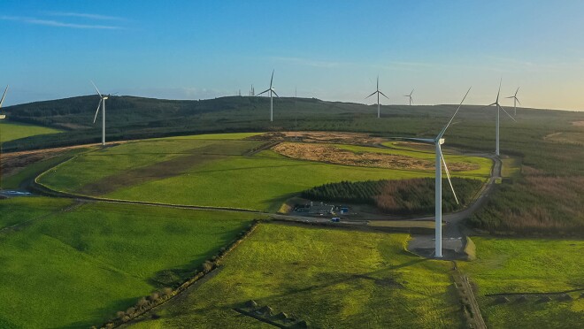 An image of a wind farm in a green field with windmills around it.