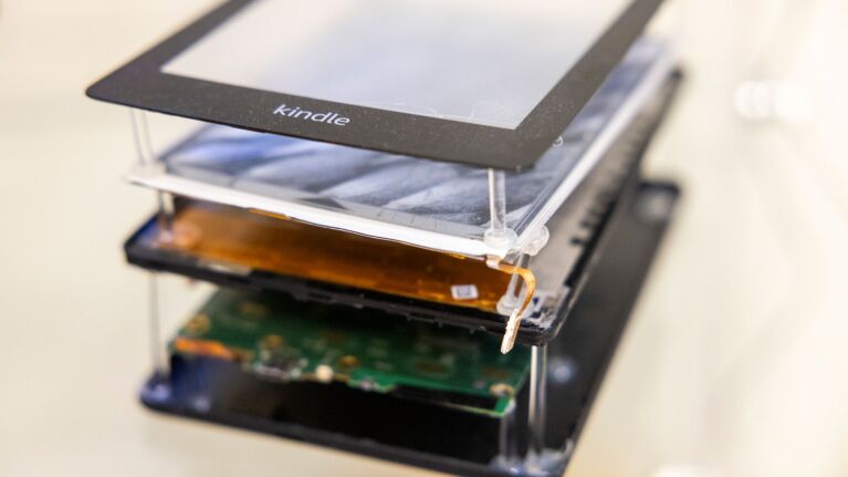 Disassembled Kindle e-reader showing screen, battery, and electronics.