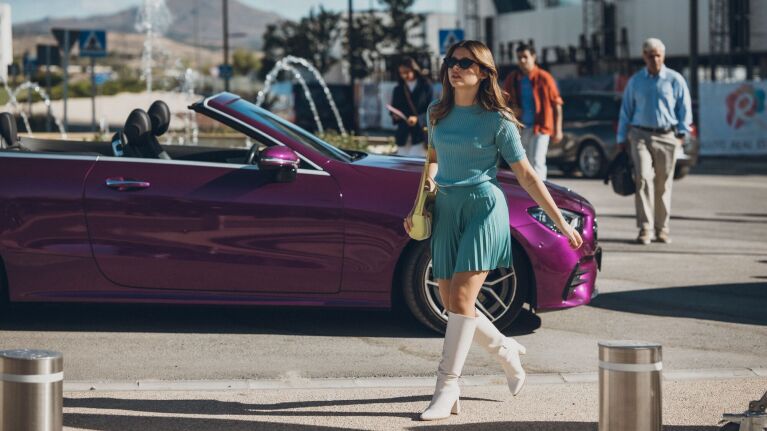 Woman in teal outfit walking confidently past purple convertible