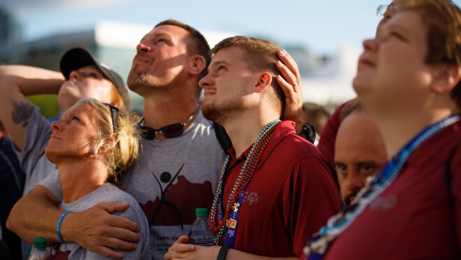 特殊奥运会参加者正在看闭幕式活动。照片中,与会者正在上升。一个男人拥抱一个女人和一个年轻的男人,因为他们都看天空。