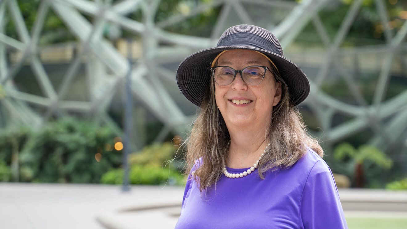 Smiling woman in purple shirt and sun hat outdoors