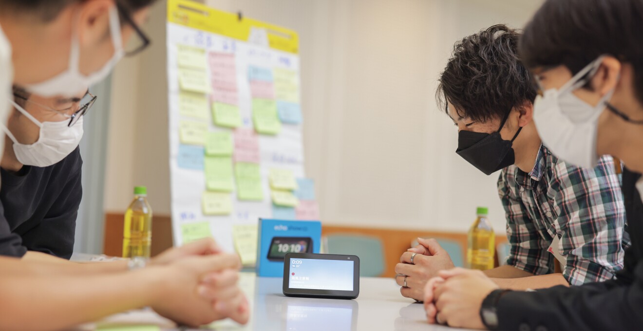 同じテーブルの4人のパパがAlexaを楽しそうに試している。