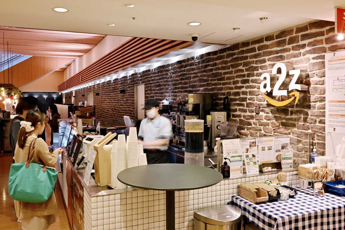 茶色いレンガの壁の前に売店のスタンド。多くの人がその前に並んでいる
