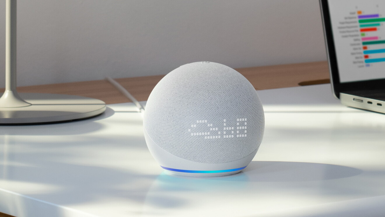 Dispositivo Alexa en una mesa de trabajo con el ordenador de fondo. 