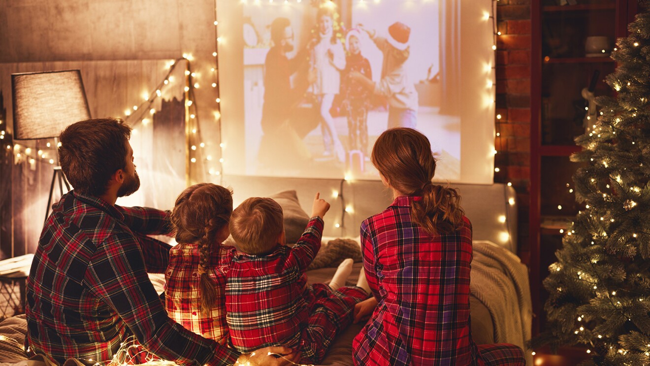 An image of a family sitting together watching a movie on a projector in a room decked out in holiday decorations