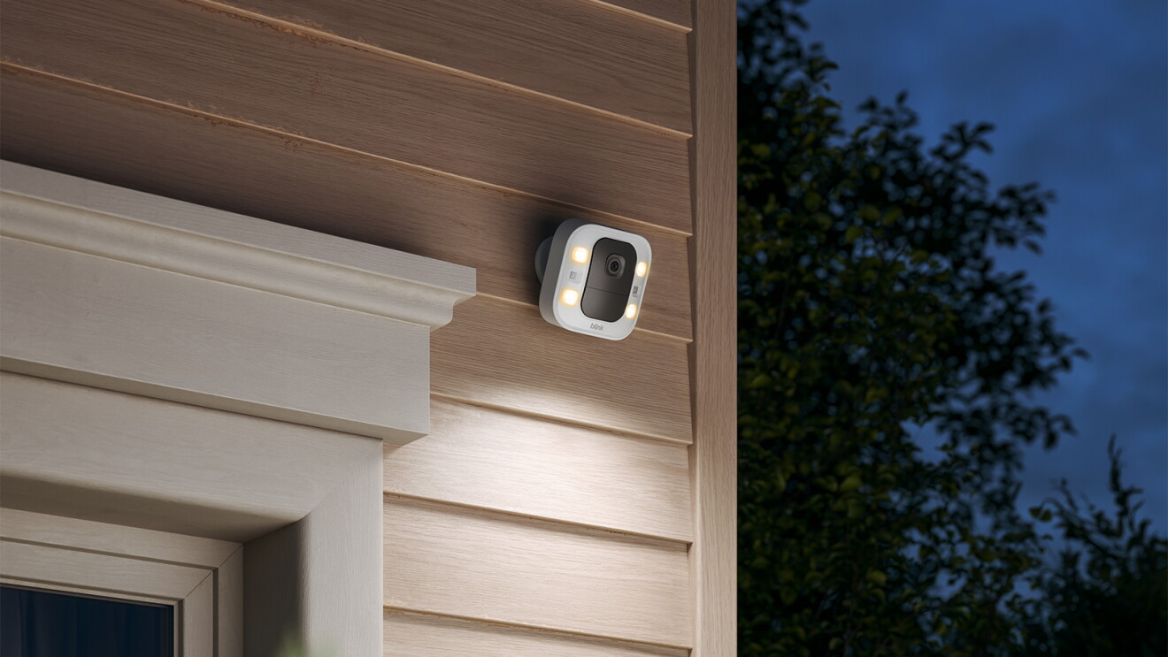 Blink Spotlight Cam 2K+, mounted on the side of a house, shining its lights at night.