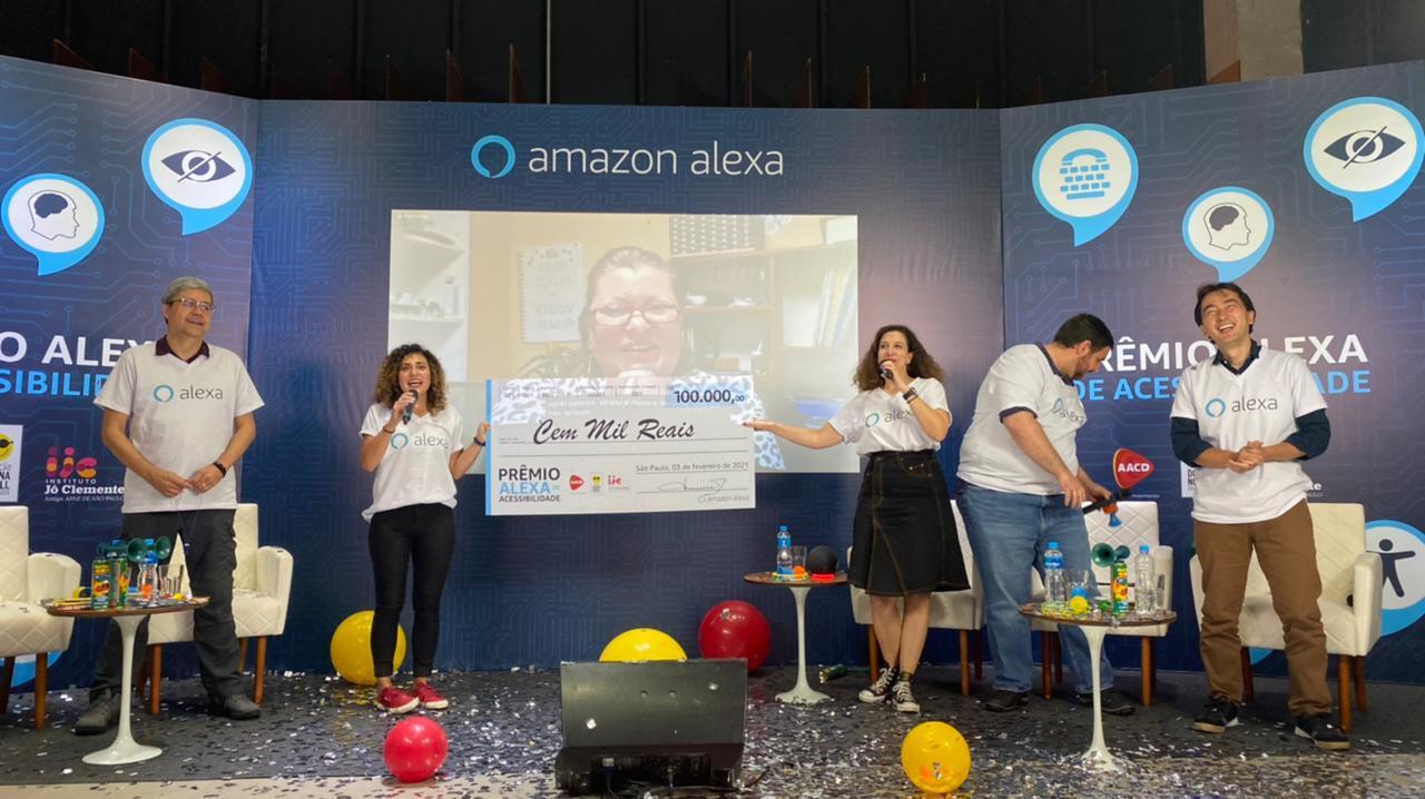 Thais, along with her colleagues, standing on a stage and honoring a winner of the Alexa Accessibility Award.