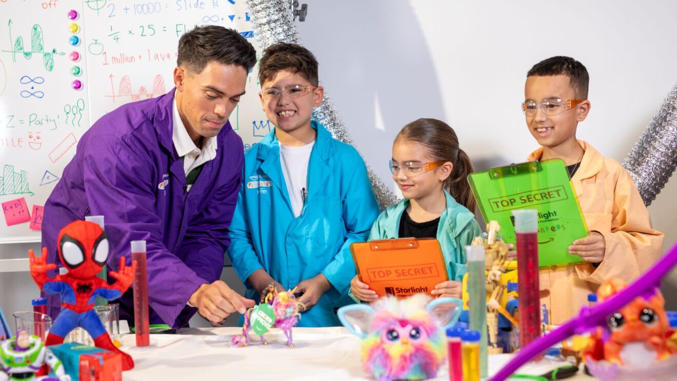 Amazon Playmakers Ambassador and Purple Wiggle, John Pearce, tests toys with three Amazon Playmakers holding colourful 'top secret' folders.