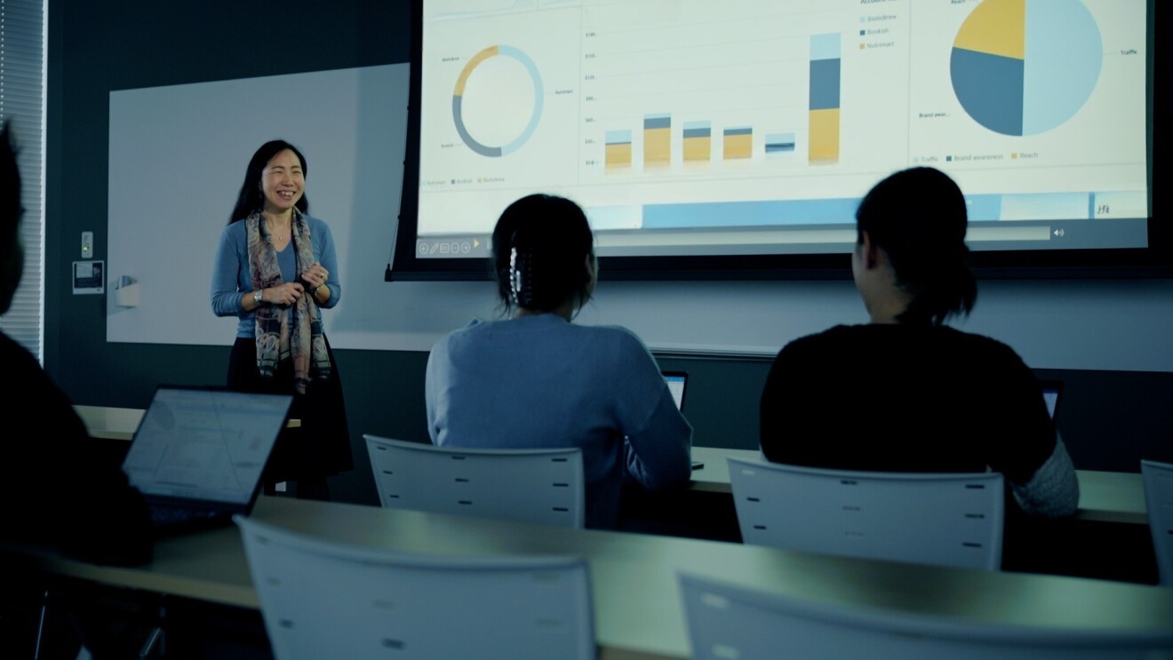 1人の女性が、暗い部屋でビジネスチャートとグラフを数人の観客に説明している
