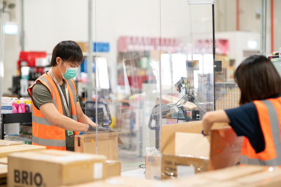 Two people can be seen working on an Amazon package with a glass barrier between them