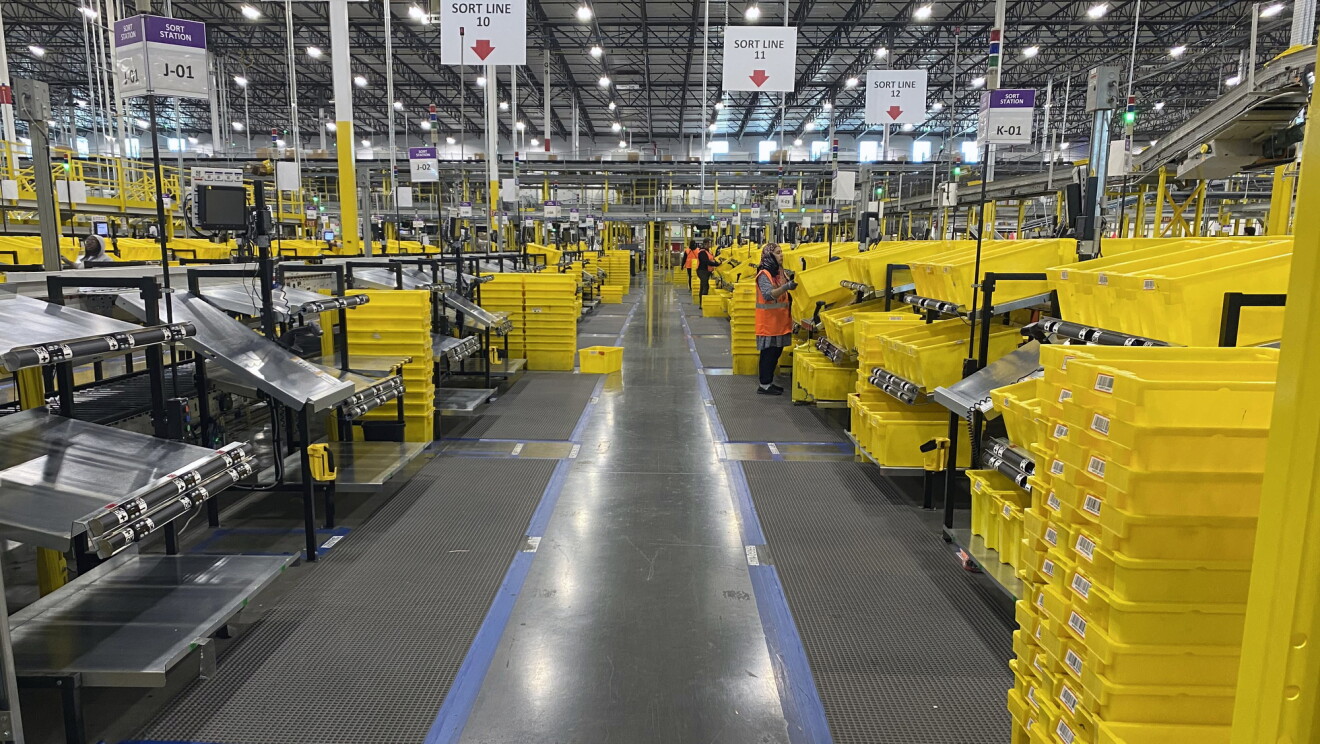 Zobacz wnętrze centrum realizacji Amazon pokazujące linie sortowania, ze współpracownikami praktykującymi dystans społeczny.