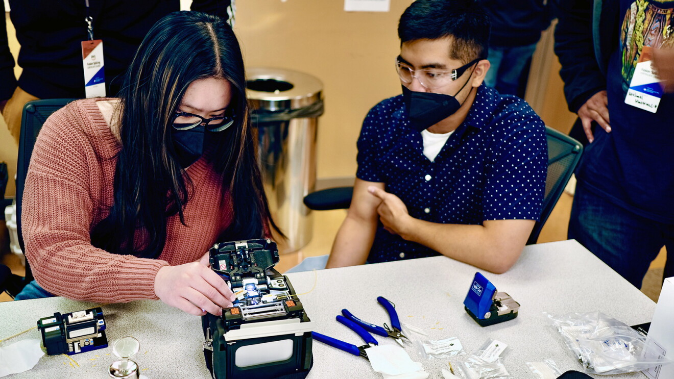 An image of two people working on a piece of technology hardware in a class setting. 