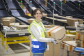 Piano americano di Ilaria di Bartolomeo, Operations Manager di Amazon a Casirate (Bergamo), mentre lavora nel centro di smistamento. Sorregge in mano un pacco con il sorriso di Amazon. 