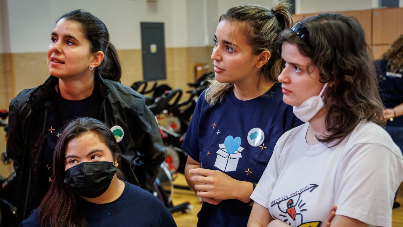 En las instalaciones de Down Madrid en Madrid aparecen 4 mujeres, dos trabajadoras de Amazon y dos participantes de la fundación. Los trabajadores de Amazon van con la misma camiseta azul y el badge colgado y los de Down Madrid con deportivas y ropa cómoda. Están todas escuchando instrucciones. 
