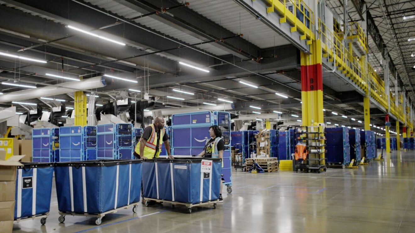 Workers in safety vests discussing near blue carts in Amazon facility