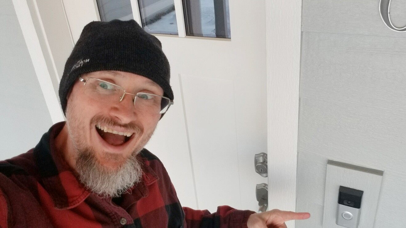 A man smiling and pointing to his Ring outside of his home.