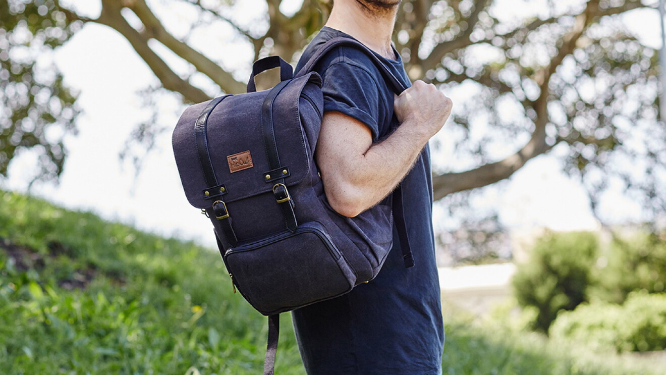 A man stands in a grassy field with a blue Hipcub backpack.