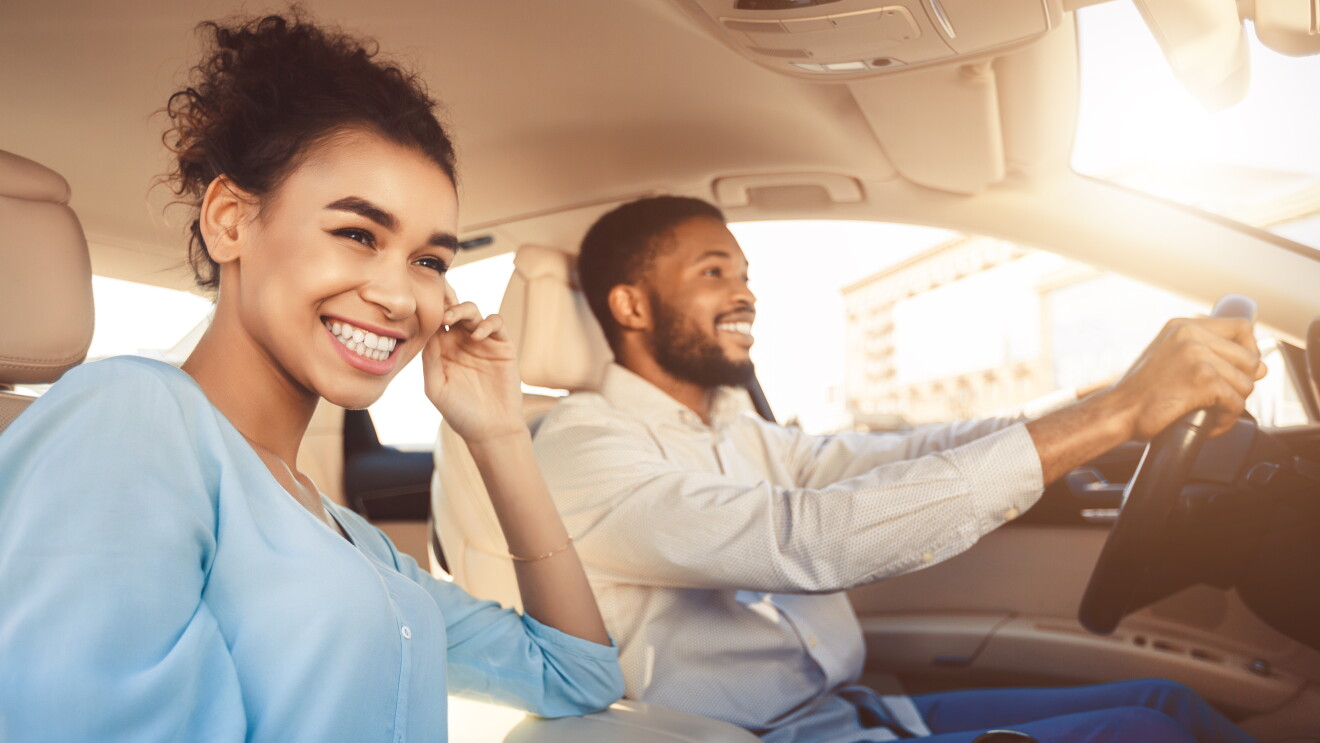 Ein Mann und eine Frau sitzen in einem Auto und lachen. Der Mann sitzt am Steuern und fährt den Wagen.