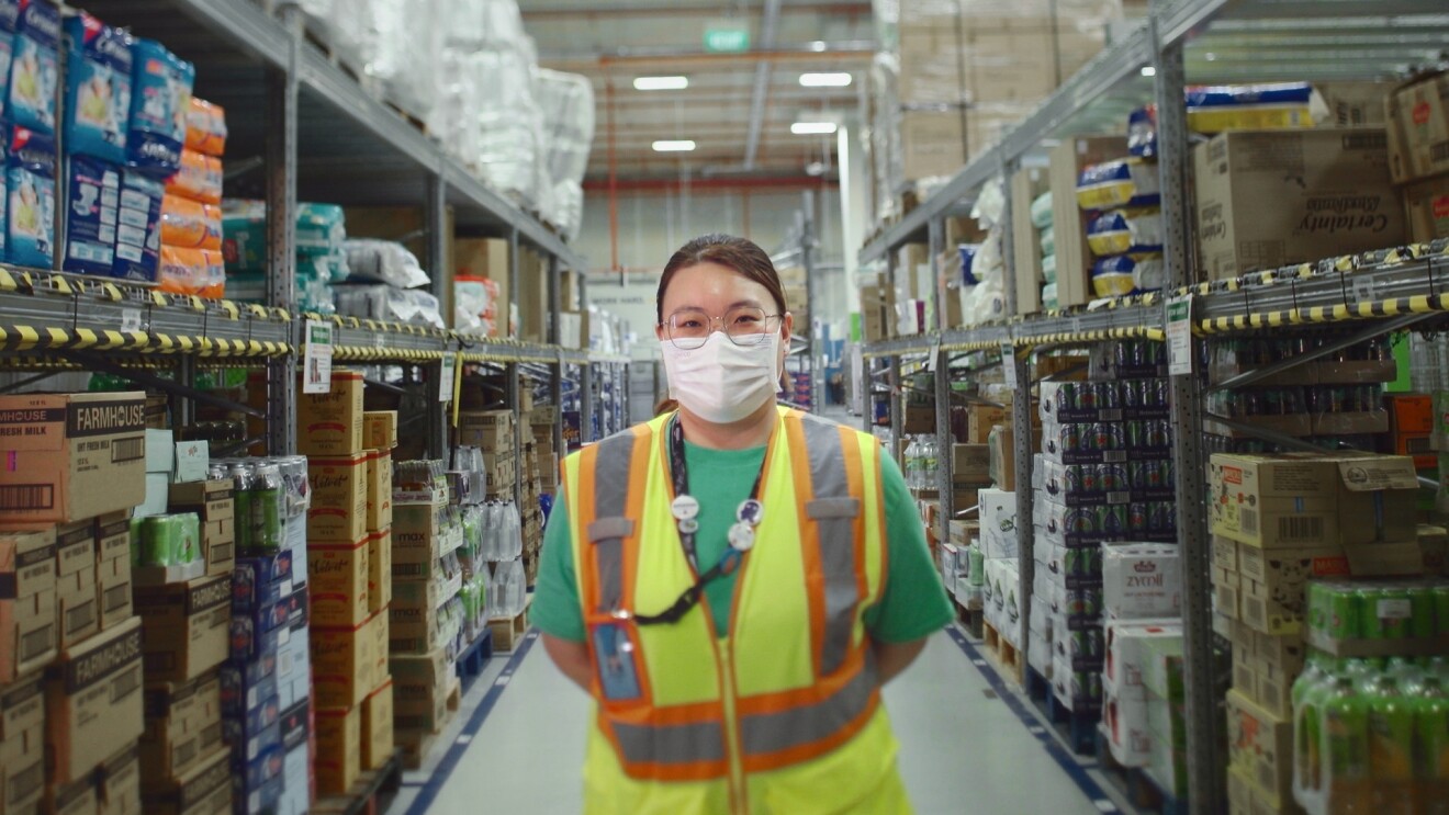 A lady is seen on the floor of a warehouse wearing a safety vest