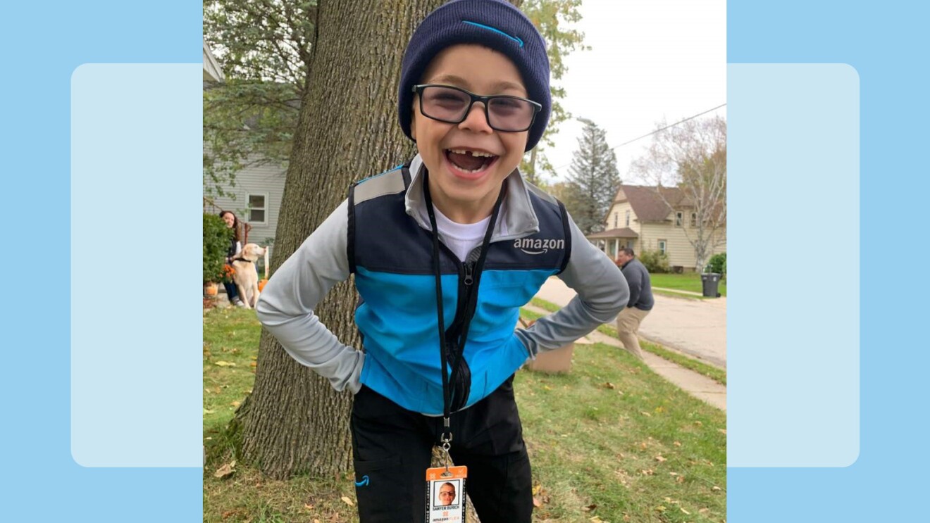 An image of a child wearing an Amazon delivery costume smiling with a blue background. 