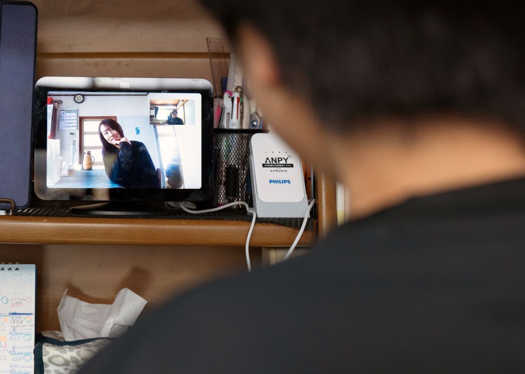 デスクのラックに置かれているデバイス(Echo Show 8)の画面に女性が映っている。画面の手前に人物(力斗さん)