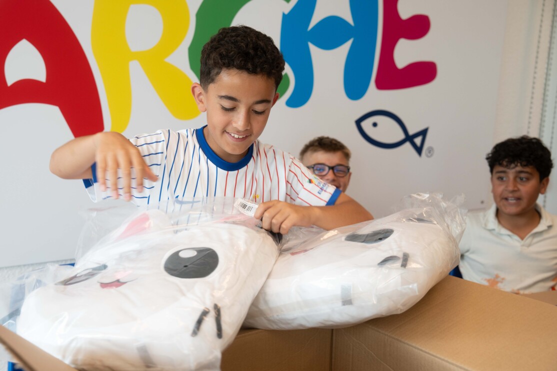 Ein Kind packt Pakete aus und steht vor der Aufschrift „Arche".