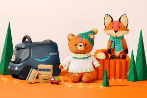 A holiday bear plush toy and a holiday fox plush toy sit next to a toy Amazon delivery vehicle with delivery boxes stacked next to it.