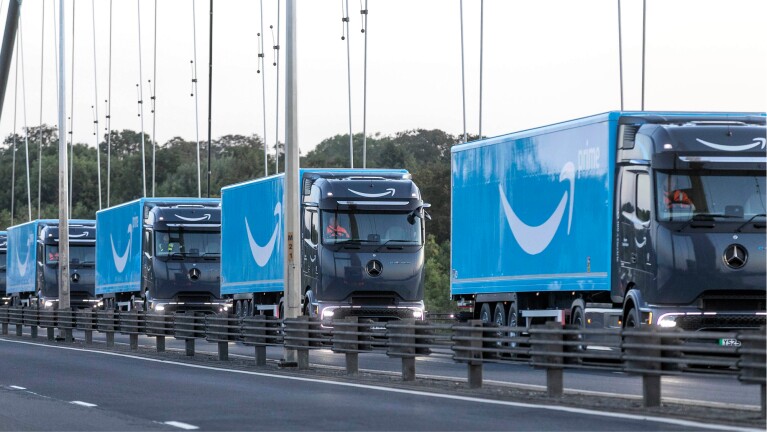 Convoy of blue Amazon trucks driving down a motorway