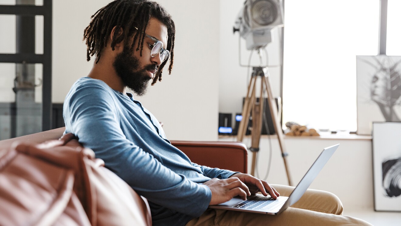 A man sits on a couch with his laptop open on his lap.