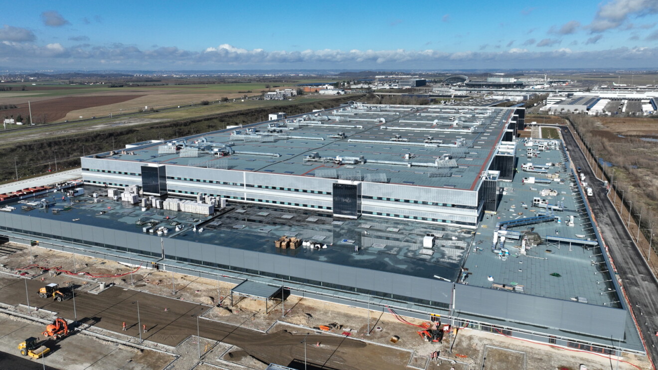 Large Amazon warehouse facility with flat roof in open area surrounded by fields