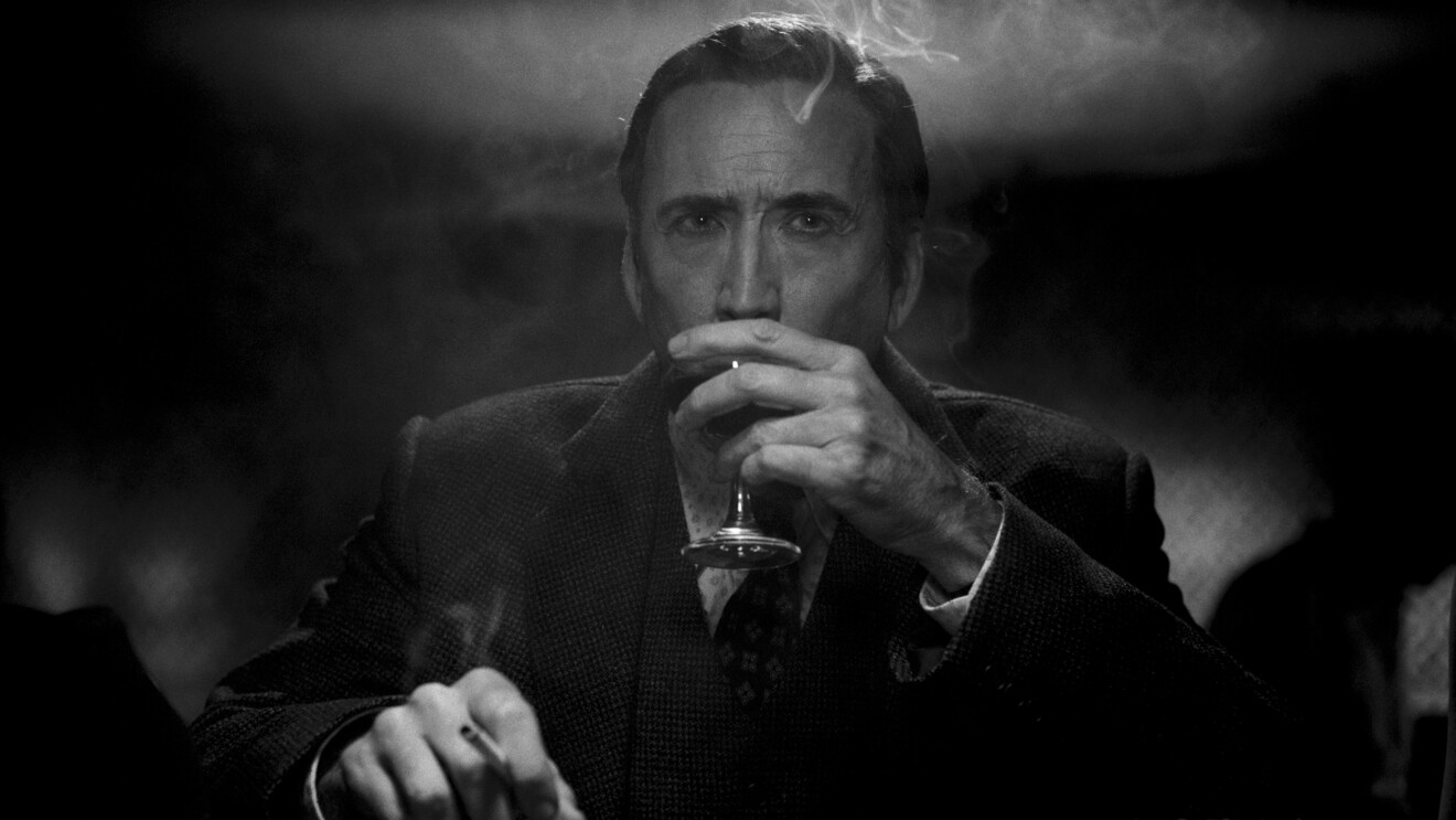 Man in suit drinks from glass, surrounded by smoke in dark setting.