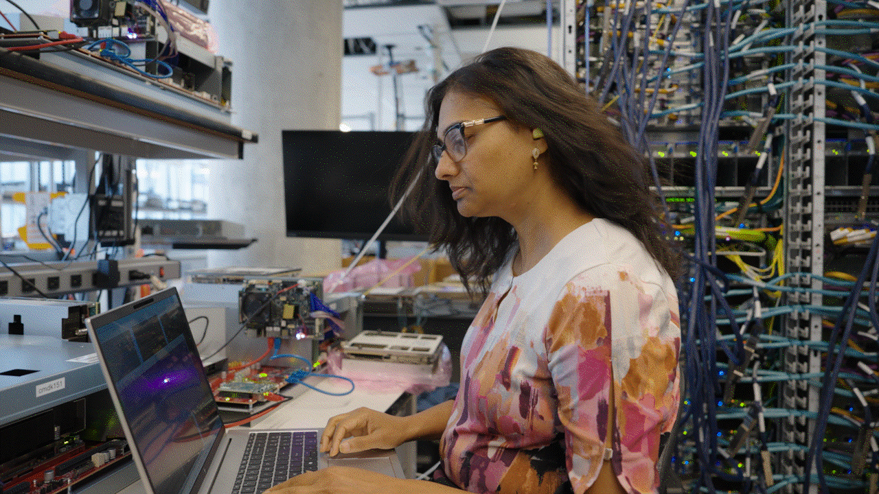 A Software Engineer in an AWS lab working on a computer with a wiring board displayed behind her