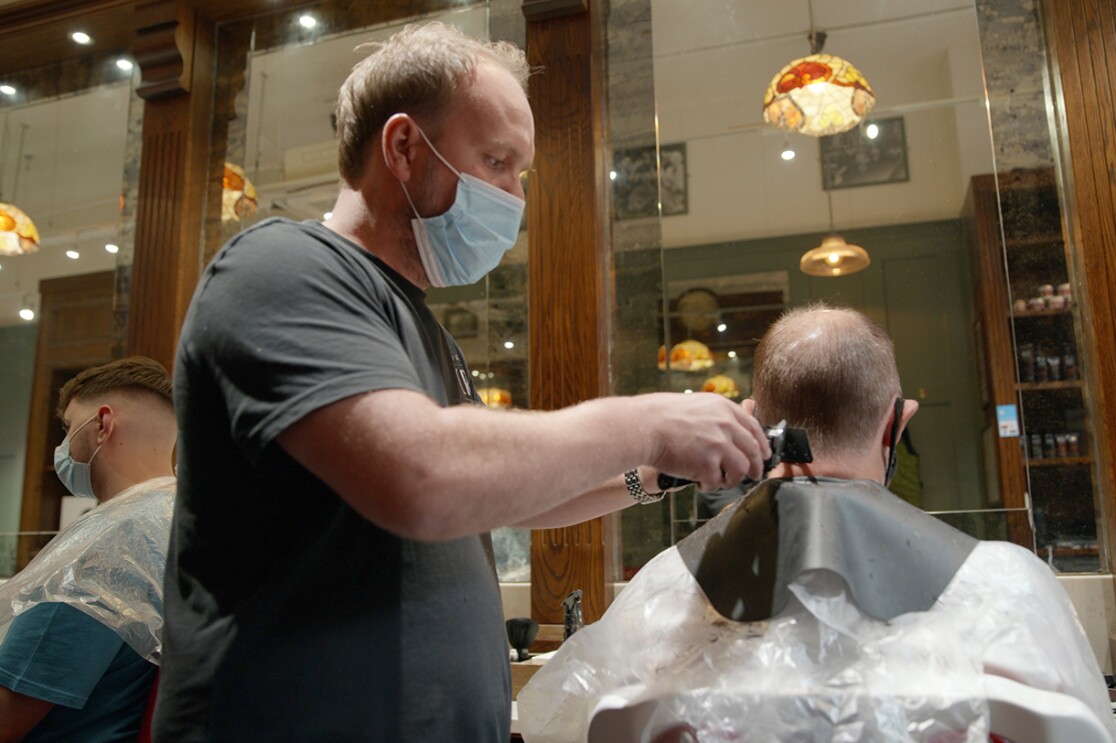 An image of a man wearing a mask while cutting another man's hair.