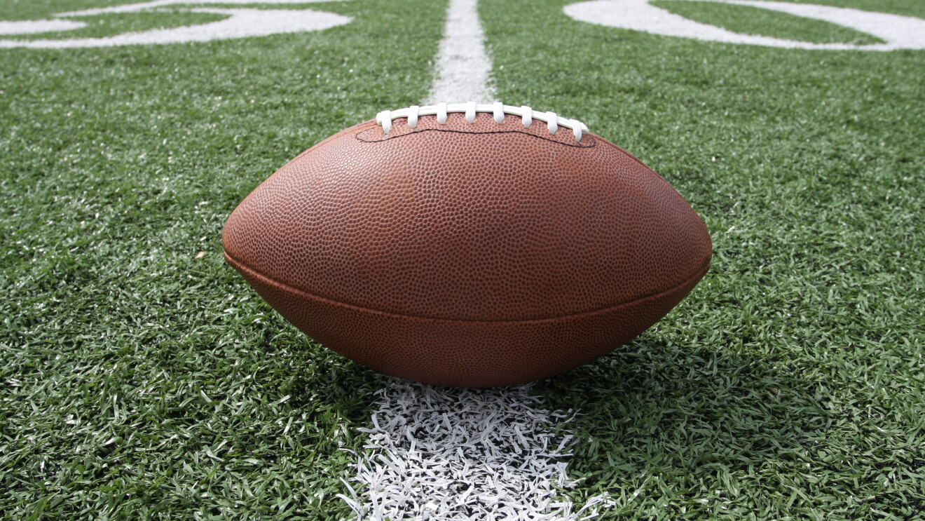 An inflated football sits on a yard line of an American football field.