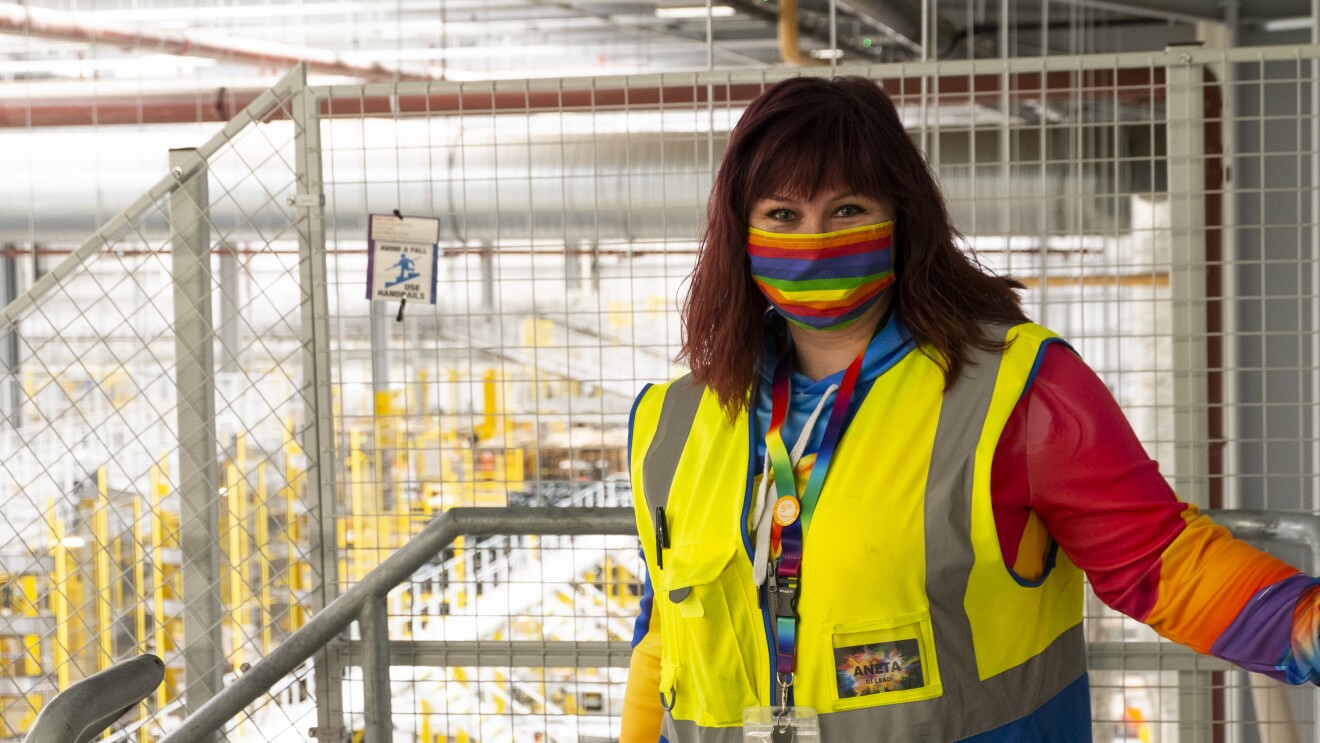 Amazon FC Lead Aneta Bachledova-Pateman wearing a yellow vest and a rainbow face mask, inside an Amazon site