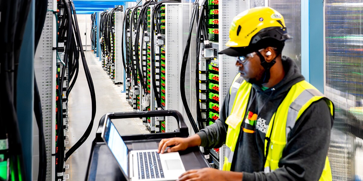 A data center technician working on a laptop device within a server room.