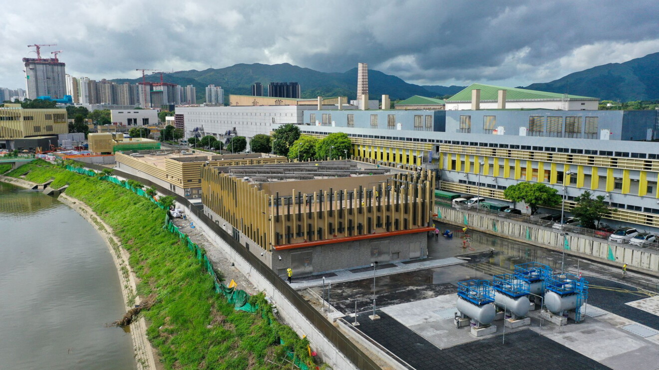 Hong Kong: Urban development along riverbank with industrial facility and mountains in background