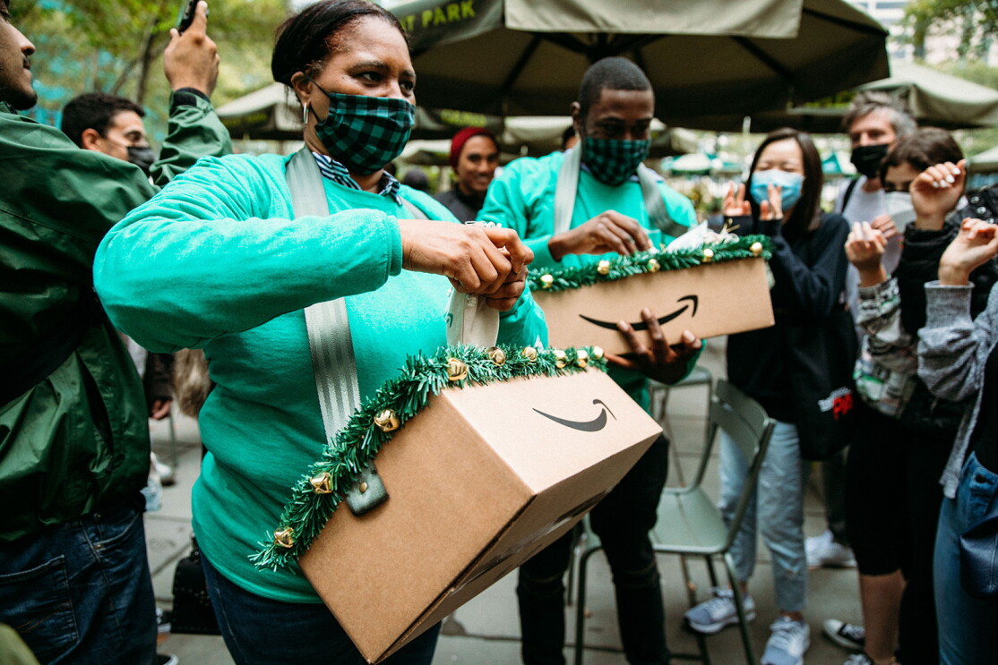 An image of a woman passing out treats to a crowd. She is waring a green Amazon shirt and a black and green checkered face mask.