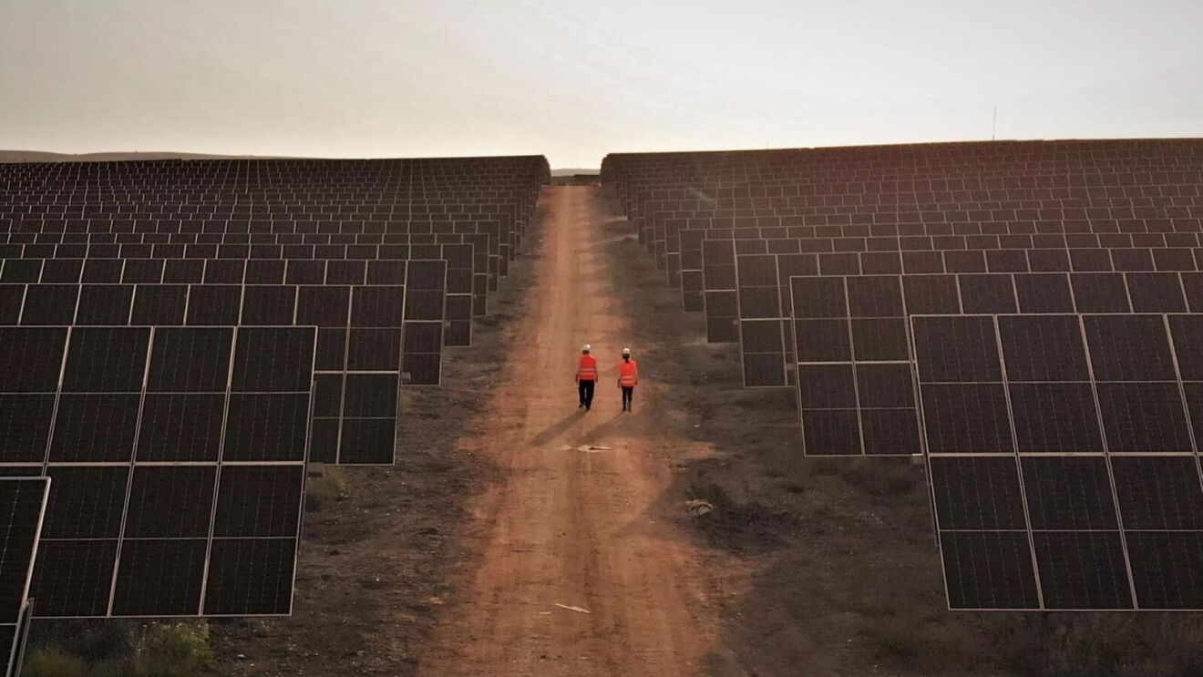 Amazon renewable: Two workers walking through vast solar panel field at dusk