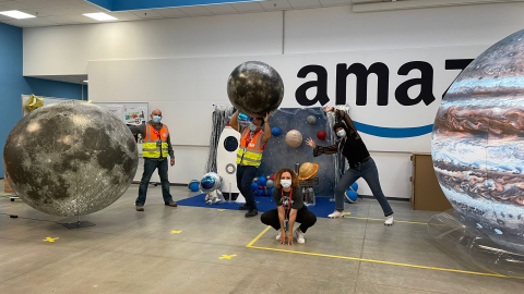 Gruppo di dipendenti Amazon posa in mezzo a riproduzioni di pianeti. 