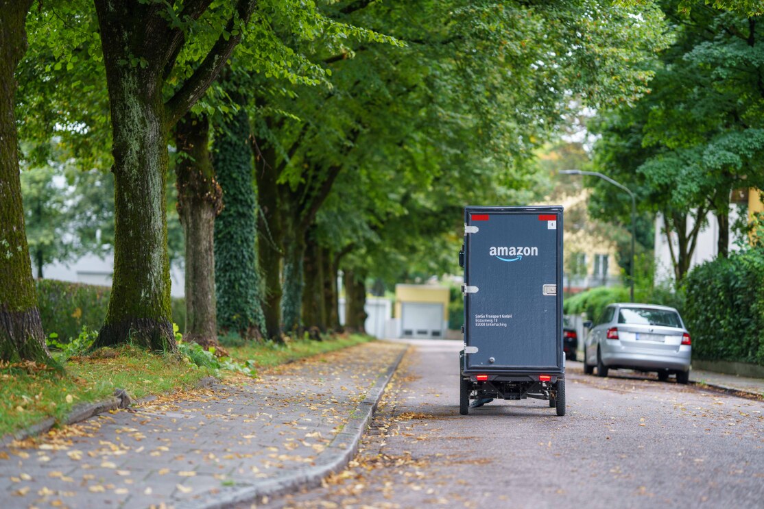 Ein E-Cargo Bike mit Amazon-Logoaufdruck fährt auf einer Baumallee.