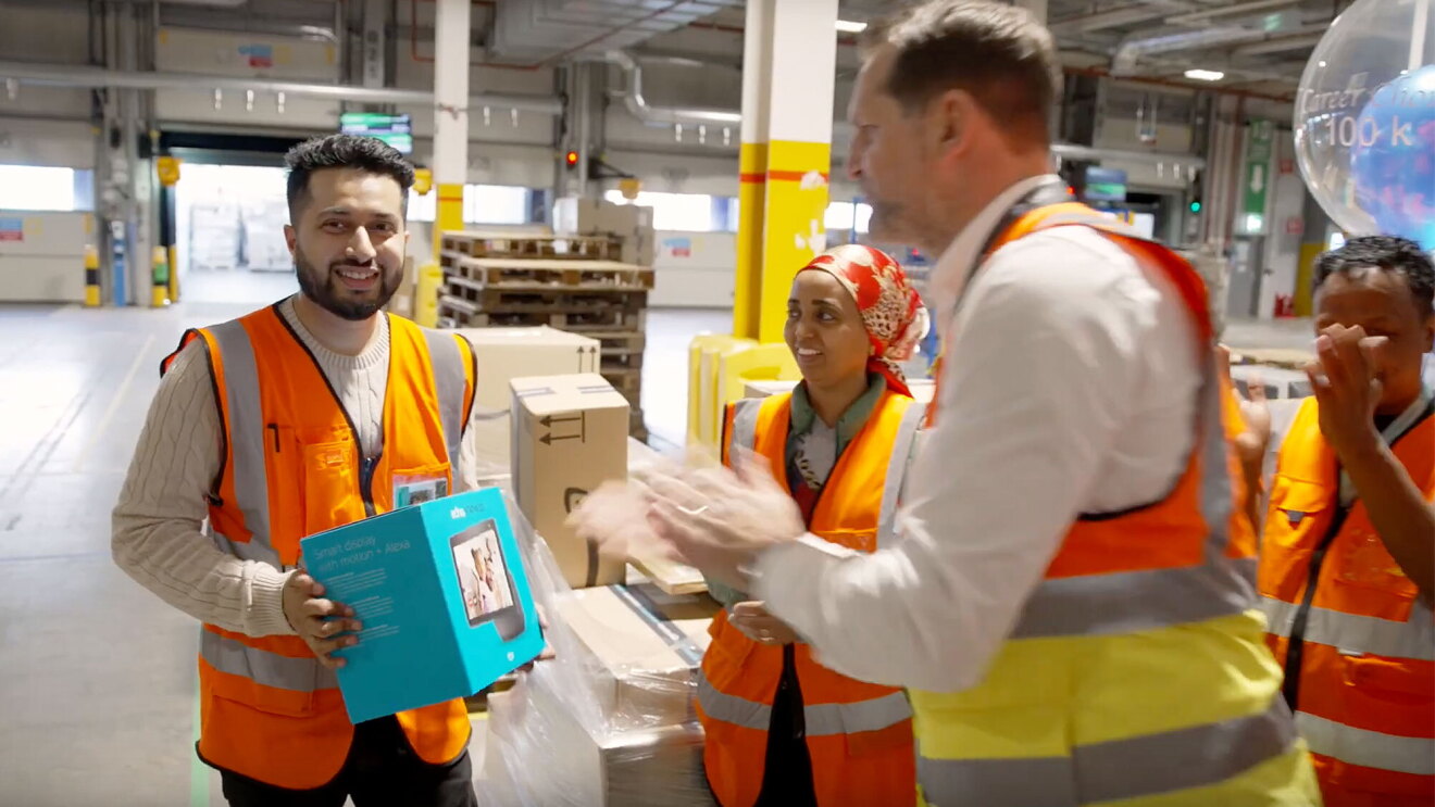 Sohil holds a gift while his team claps in an Amazon fulfillment center.