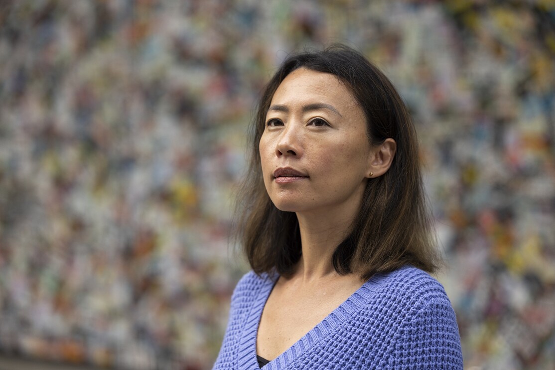 An image of a woman smiling for a photo in front of a blurred, multi-colored background.