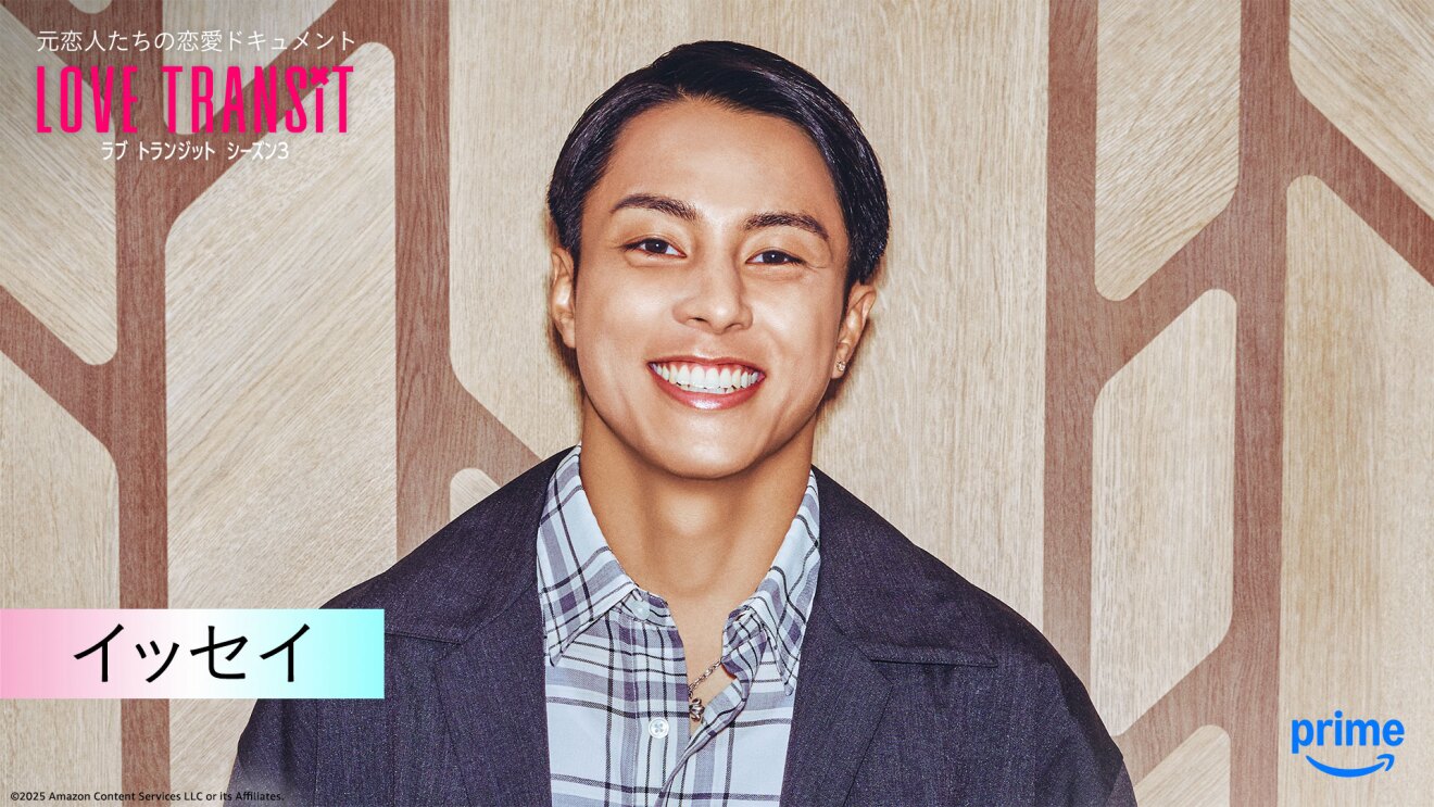 木目調の壁の前に立つ人物のバストアップ。出にもジャケットにチェックのシャツを着用。左上隅に「LOVE TRANSIT」の文字。左下に「イッセイ」と名前が表示されている。