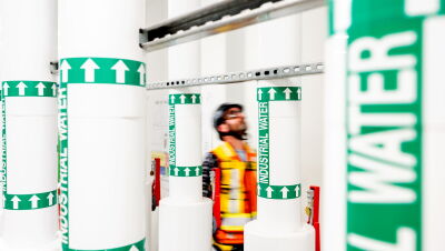 Worker in safety vest amid industrial water pipe labels
