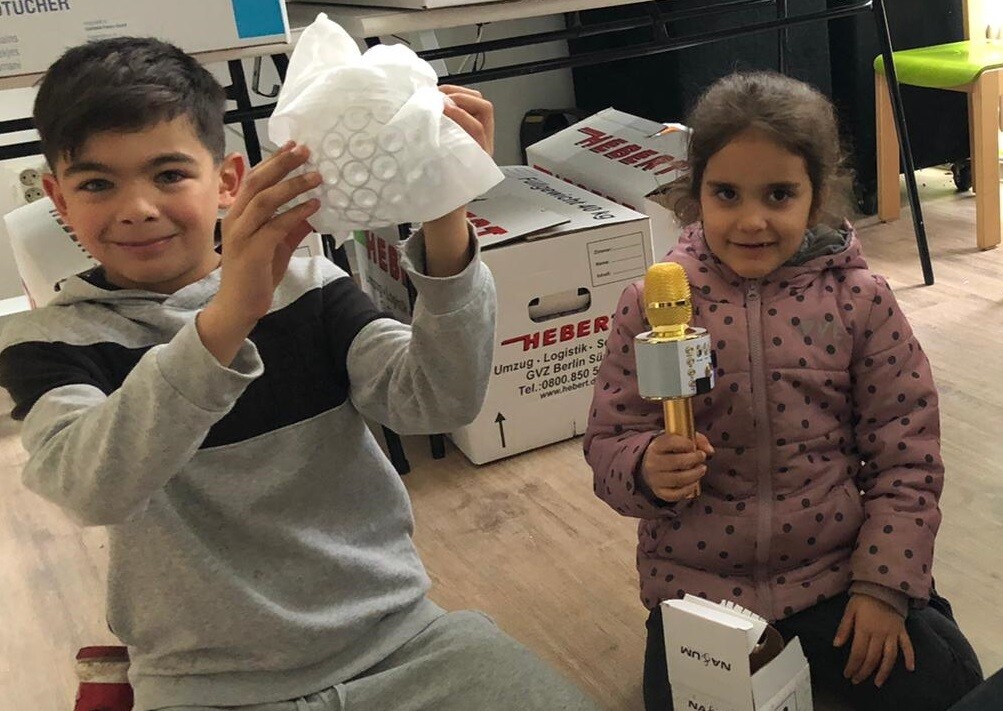 Ein Junge hält ein halb ausgepacktes Geschenk, während sich ein Mädchen über ein goldenes Mikrophon freut.