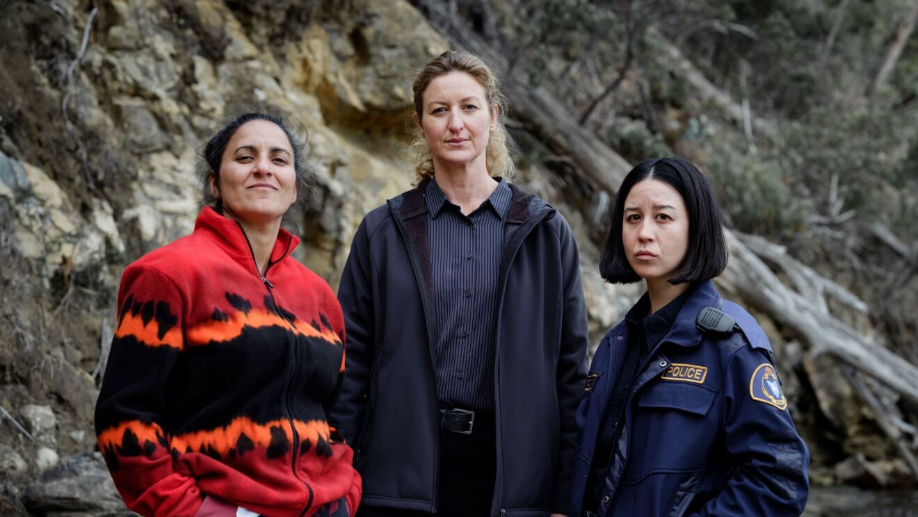 three women standing next to each other. from left, a woman in red jacket, a woman in stripe navy shirt and jacket, and short-haired policewoman.