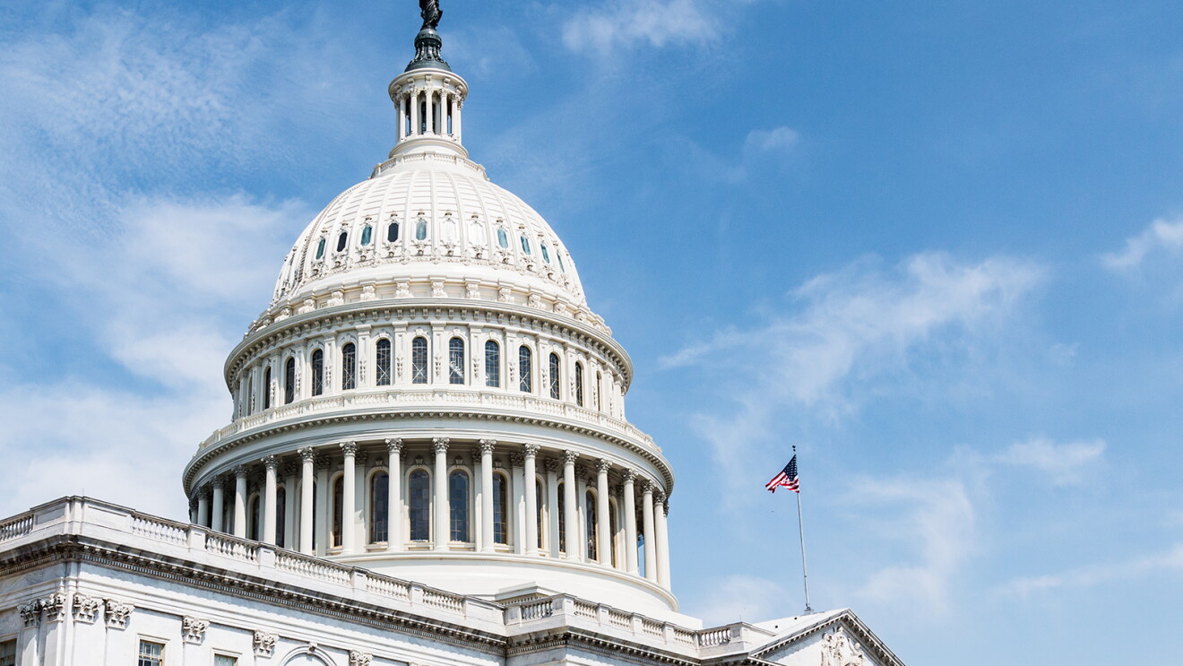 An image of the United States Capitol Building, home of Congress. There is a blue sky behind the building and an American flag flying on its roof.