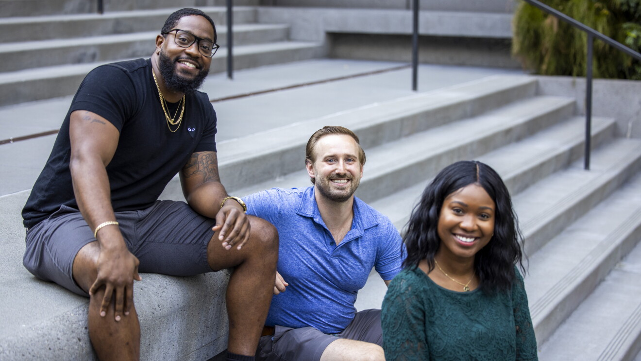 Two women and a man sit on a concrete staircase.