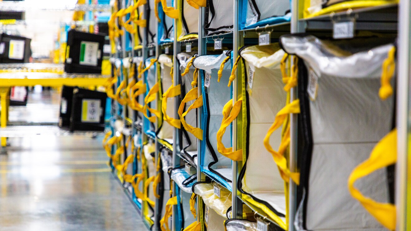 Estantería de un centro logístico con bolsas que tienen las asas de color amarillo. Las estanterías tienen cuatro pisos y más de 10 bolsas.